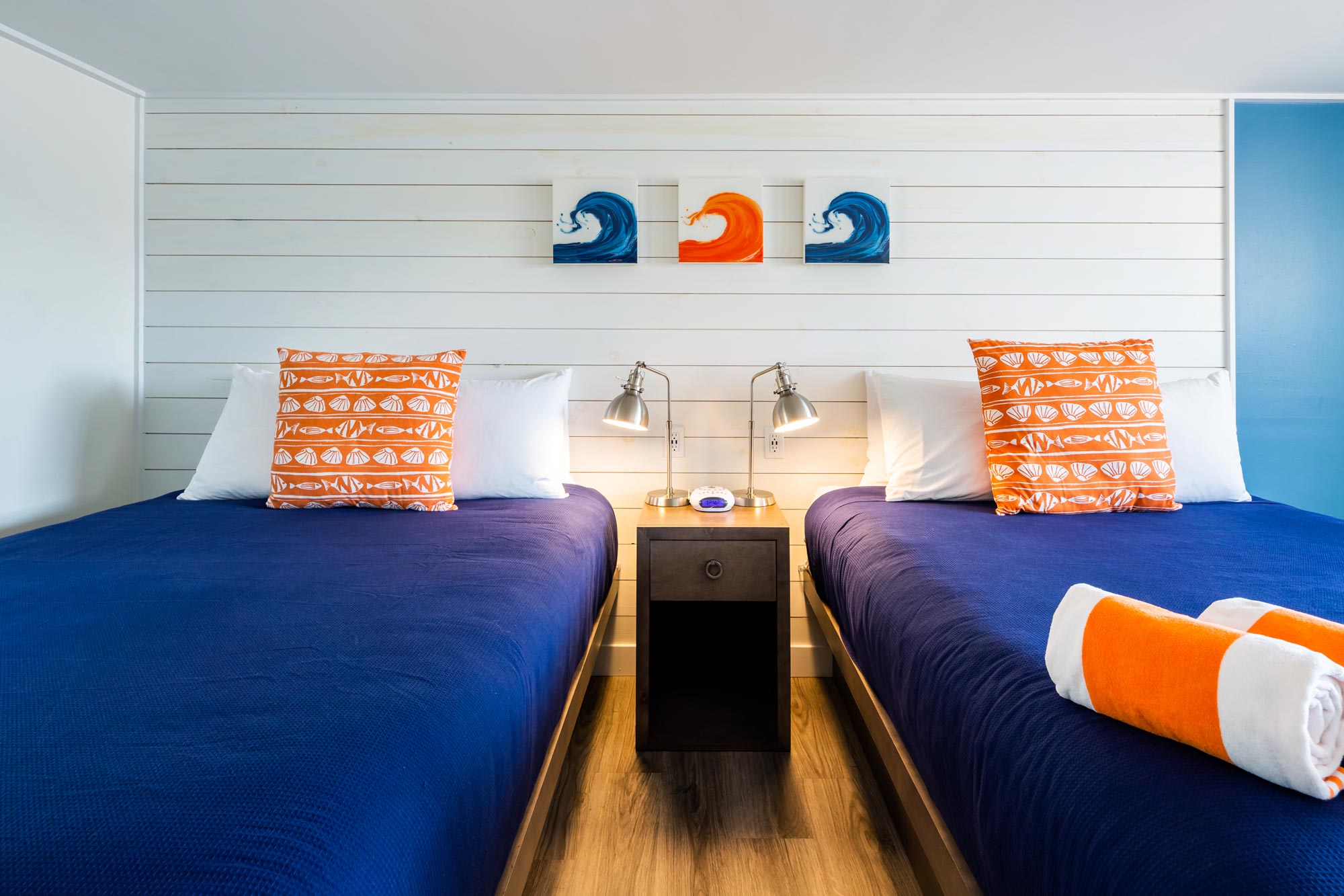 Two hotel beds with bright pillows that match the art