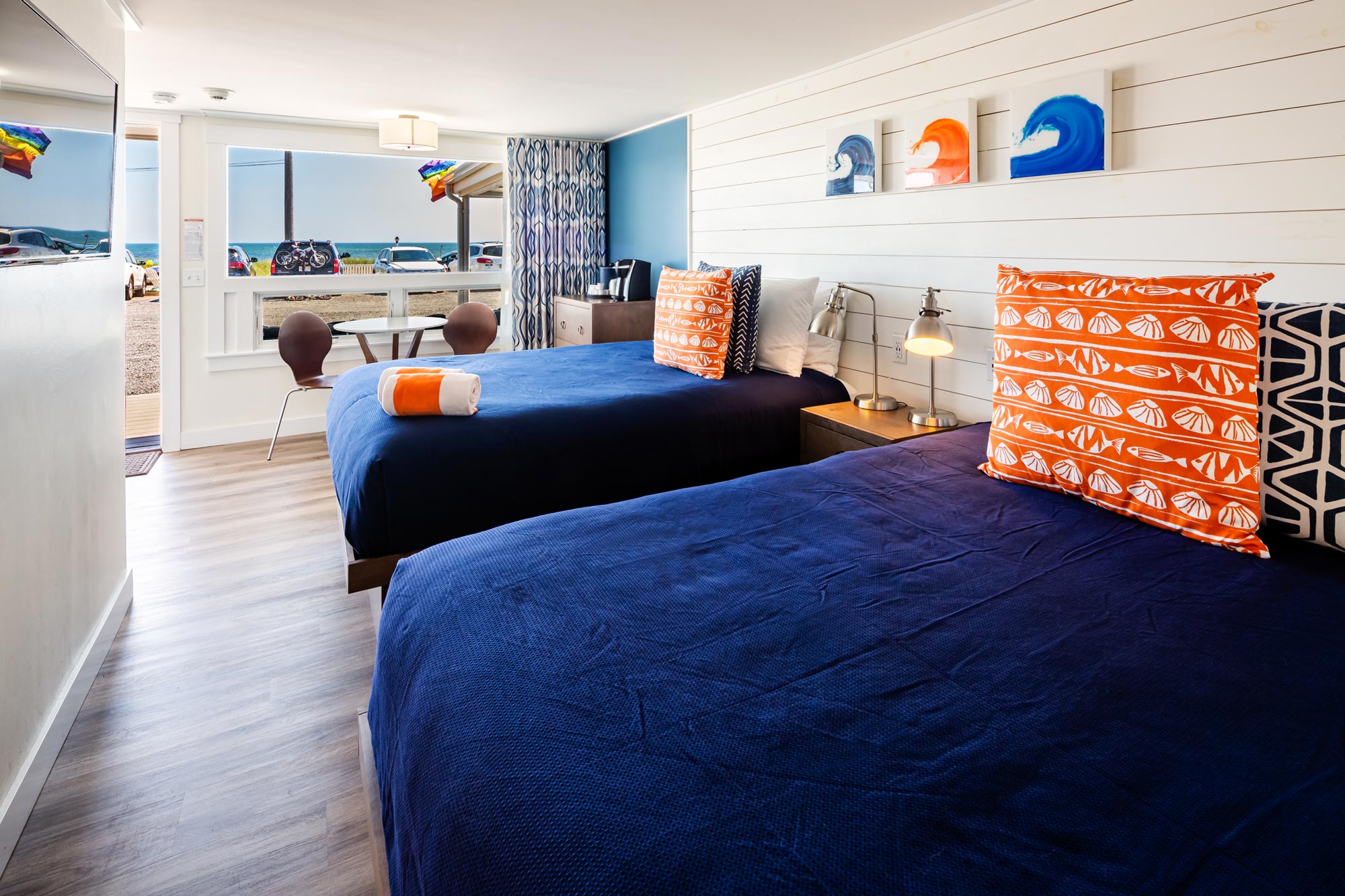 Two hotel beds with bright pillows that match the art